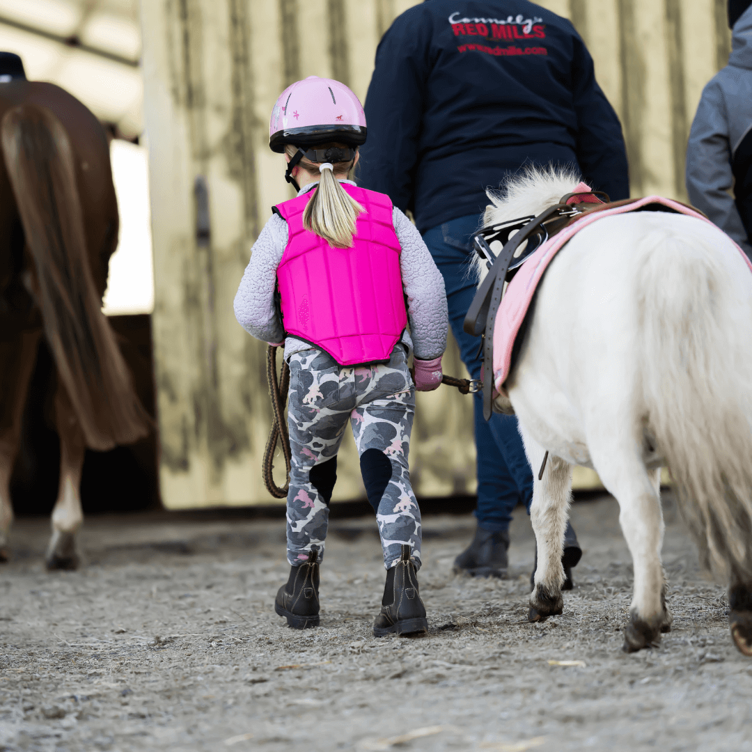 Barn med rosa säkerhetsväst leder liten vit ponny